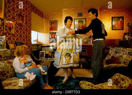 Elvis Presley Fan Familie, Mrs Debbie Constable und ihre Tochter Lisa Marie Holding Tochter. Sie ist nach Presleys einziger Tochter Lisa Marie Presley benannt. Mrs. Constable tanzt mit Chris, ihrem Schwiegersohn, zu Elvis Records im Wohnzimmer ihres Hauses im Süden Londons. Mrs. Constable trägt ein Elvis-Kleid und Elvis-Portrait-Ohrringe. Fotos des King of Rock and Roll -Elvis Presley schmücken die Innenausstattung der Wohnungen. Tooting, South London, England um die 1995 1990er Jahre, UK HOMER SYKES Stockfoto