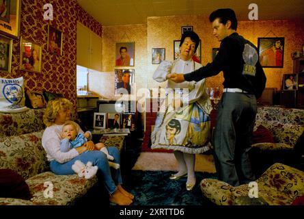 Elvis Presley Fan Familie, Mrs Debbie Constable und ihre Tochter Lisa Marie Holding Tochter. Sie ist nach Presleys einziger Tochter Lisa Marie Presley benannt. Mrs. Constable tanzt mit Chris, ihrem Schwiegersohn, zu Elvis Records im Wohnzimmer ihres Hauses im Süden Londons. Mrs. Constable trägt ein Elvis-Kleid und Elvis-Portrait-Ohrringe. Fotos des King of Rock and Roll -Elvis Presley schmücken die Innenausstattung der Wohnungen. Tooting, South London, England um die 1995 1990er Jahre, UK HOMER SYKES Stockfoto