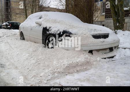 Ein im Winter auf der Straße geparkter PKW, der von der Schneeräumungsanlage mit Schnee bedeckt ist. Ein Auto, das im Schnee vergraben ist Stockfoto