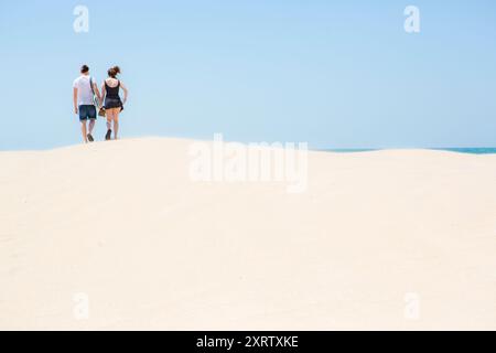 Weiße Sanddünen bei starkem Wind an der Küste Spaniens, Conil de le Frontera, mit 2 jungen Leuten, einem männlichen adm und einer weiblichen, die über den Kamm laufen. Stockfoto