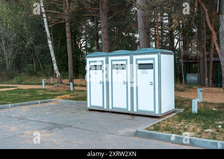 Eine Reihe mobiler Toiletten im Freien in einem Park, perfekt für Parkeinrichtungen und öffentliche Veranstaltungen. Die Kabinen sind sauber und gepflegt, professionell Stockfoto