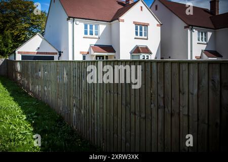 Weiß gestrichene Häuser in der Sonne hinter einem langen Holzzaun. Stockfoto