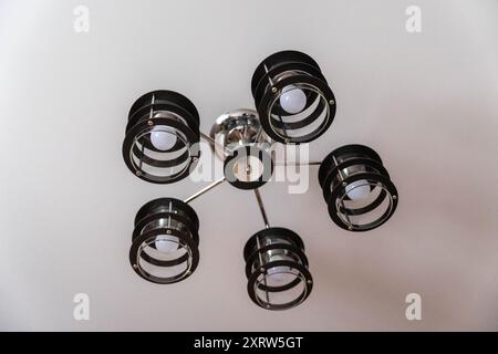 Ein schwarz-verchromter Kronleuchter mit fünf Lampen hängt von einer weißen Decke. Stockfoto