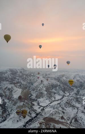 Heißluftballons treiben bei Sonnenaufgang über eine schneebedeckte Landschaft Kappadokiens und schaffen eine surreale und magische Winterszene Stockfoto