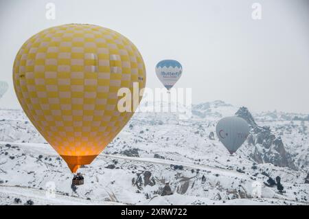 Heißluftballons schweben bei Sonnenaufgang über Kappadokiens schneebedeckten Täler und bieten atemberaubende Winterlandschaften in dieser berühmten türkischen Region Stockfoto