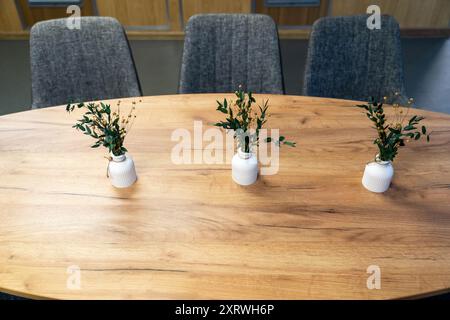 Drei Vasen mit Grün auf einem Holztisch in einem Innenbereich. Stockfoto