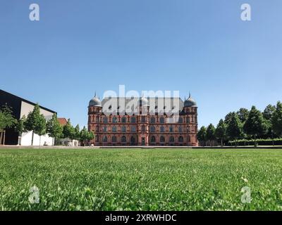 Ein großes Gebäude mit grünem Rasen davor. Das Gebäude ist alt und hat viele Fenster. Der Rasen ist üppig und grün und der Himmel ist klar und Stockfoto