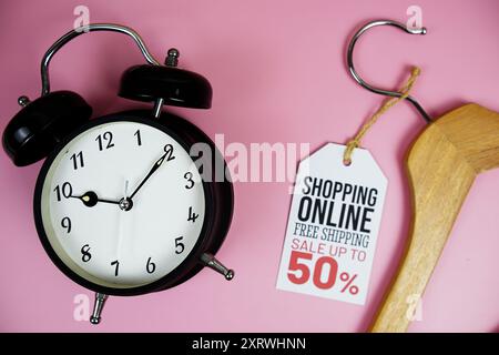 Shopping Online Sale bis zu 50 % Rabatt auf den Preis mit Kleiderbügel aus Holz und Wecker von oben auf rosa Hintergrund Stockfoto