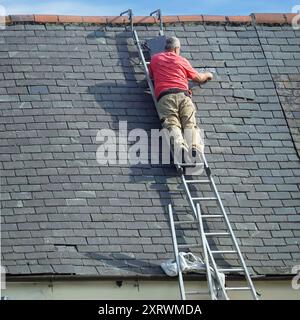 Rückansicht Handwerker, der in scheinbar prekärer Position arbeitet und ausgewählte beschädigte Schiefer auf dem schrägen Dach des Grundstücks im County Durham England, Großbritannien, ersetzt Stockfoto