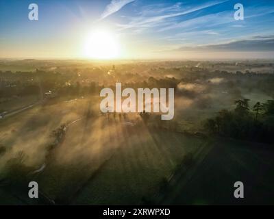 Landschaftsfotografie der Stadt Cirencester in den Cotswolds während der Sonnenaufgang über nebeligen Feldern an einem Wintermorgen. Stockfoto