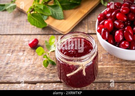 Kornelkirsche, Dogwoods essbare Beerenmarmelade oder Marmelade im kleinen Glas mit frischen Beeren auf Holztisch, Kopierraum Stockfoto