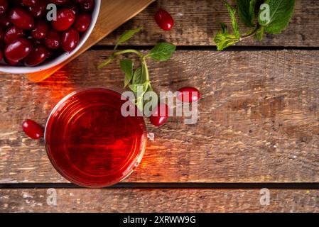 Kornelkirsche, Harthölzer essbarer Beerensaft oder Likör im Glas, auf Holztischhintergrund, mit Minze- und frischen cornus-Beeren Kopierraum Stockfoto