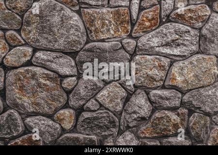 Eine Wand aus Stein mit rauer Textur. Die Wand besteht aus Steinen unterschiedlicher Größe, und die Steine sind so angeordnet, dass sie ein Muster erzeugen Stockfoto