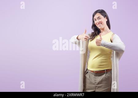 Porträt einer glücklichen und selbstbewussten jungen Geschäftsfrau mit zwei Daumen nach oben auf violettem isoliertem Hintergrund Stockfoto
