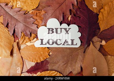 Ein weißes Schild mit der Aufschrift Buy Local steht auf einem Haufen Blätter. Herbstkonzept und Idee der Unterstützung lokaler Unternehmen Stockfoto