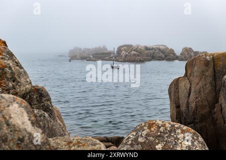 Kleines hölzernes Fischerboot, das an einem nebeligen Sommertag langsam auf der Ria de Pontevedra fährt. Stockfoto