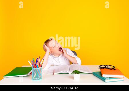 Foto von hübschen charmanten süßen verschlafenen Jungen sitzen Schreibtisch wollen Schlaf Hausaufgaben Übungen isoliert auf gelbem Hintergrund Stockfoto