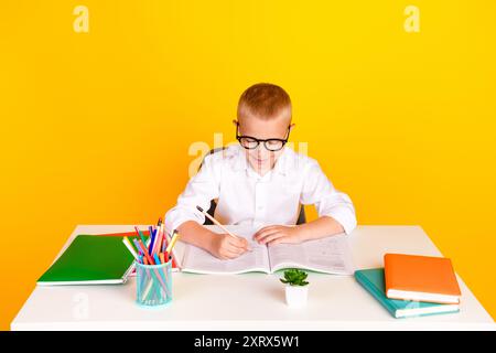 Foto des cleveren süßen charmanten Jungen tragen weißes Hemd schreiben Hausaufgaben isoliert auf gelbem Hintergrund Stockfoto