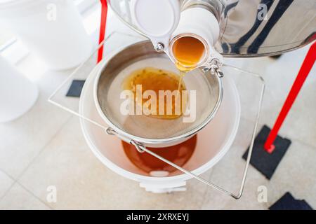 Frischer Honig fließt aus einem Fassstopfen in die Filtration Stockfoto