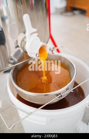 Bienenzuchthonig, der aus dem Bienenstock gewonnen wird, fließt aus einem Fass in das Sieb zur Filtration Stockfoto