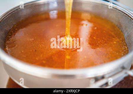 Viscouse Golden Bee Honig tropft und fließt in Einen Pool Honig, der von einem Sieb filtriert wird Stockfoto