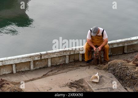 Fisherman arrangiert Fischernetze am Rand seines Fischerbootes, das nach einer Fahrt im Hafen angedockt ist. Überall angeln. Stockfoto