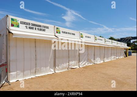 Viladecasn, SPANIEN - 12. AUGUST 2024: Messe Sant Isidro in Viladecans mit weißen Kabinen, Bäumen und Gebäuden im Hintergrund, unter teilweise bewölktem Ski Stockfoto