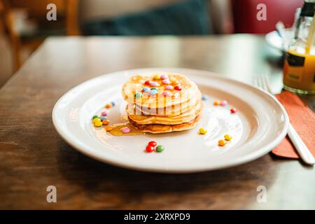 Frühstücksteller mit kleinem Stapel Pfannkuchen, belegt mit bunter Schokoladenlinse und Honig Stockfoto