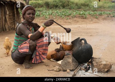 Eine junge Frau aus der Banna-ethnischen Gruppe gießt ein kaffeähnliches Getränk aus einer Tongefäß in eine Kürbisschale im südlichen Omo Valley, Äthiopien Stockfoto