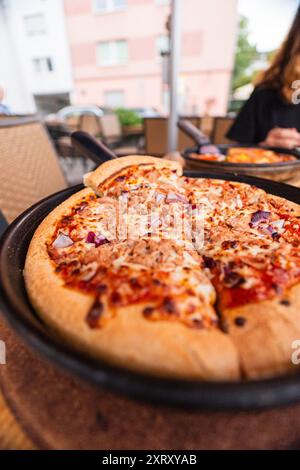 Thunfisch-Pizza in einer Pfanne frisch gebacken aus dem Ofen stehend auf einem Holztisch geschnitten und serviert mit Käse und Zwiebeln Stockfoto