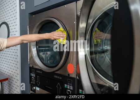 Nicht identifizierter Mann, der die Waschmaschine mit Waschmittel im Selbstbedienungswaschsalon abwischt Stockfoto