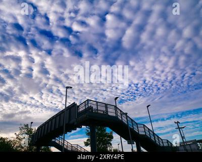 Das erste Licht mit dramatischer Wolkenlandschaft aus Altocumulus beleuchtet die Brücke über die Gleise am Radley Bahnhof Ich liebe es, den Himmel zu sehen. Was man sieht, ist oft schön und ändert sich ständig; man sieht nie zweimal denselben Himmel. Wenn ich an den meisten Orten herumspaziere, bin ich normalerweise die einzige Person, die nach oben schaut; alle anderen sind mit Köpfen nach unten und gehen ihrem täglichen Geschäft nach. Sie wissen nicht, was ihnen fehlt. Stockfoto