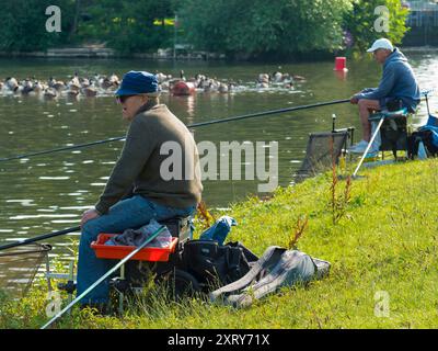 Fischer und eine Herde Kanadageesen auf der Themse bei Abingdon, nur bei Abingdon Lock und Weir. Branta canadensis ist in den arktischen und gemäßigten Regionen Nordamerikas beheimatet und wurde erfolgreich in Großbritannien eingeführt. Sie ist heute fast überall an der Themse zu sehen. Die Fischer sind an den Fischen interessiert, nicht an den Vögeln. Stockfoto