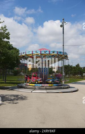 Viladecasn, SPANIEN - 12. AUGUST 2024: Buntes Kinderkarussell in einem sonnigen Park, mit einem roten Feuerwehrwagen und einem rosafarbenen Wagen. Ideal für die Werbung für Familien Stockfoto