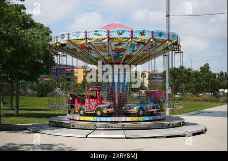 Viladecasn, SPANIEN - 12. AUGUST 2024: Kinderkarussell stoppte in einem Park mit klarem Himmel. Ein roter Feuerwehrwagen und ein rosafarbener Schwimmer heben sich zwischen grünem Tre hervor Stockfoto