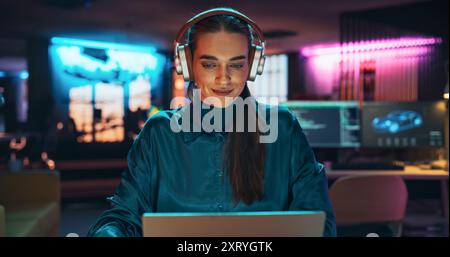 Junger Projektmanager mit Kopfhörern, der in kreativen Büroumgebungen an Laptops arbeitet. Beautiful Female Specialist schreibt Geschäftsstrategie und verwendet ein digitales Tablet, um Notizen zu machen Stockfoto