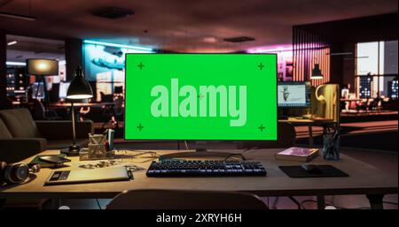 Desktop-Computer mit Mock-Up Green Screen Chroma Key Display auf dem Schreibtisch im leeren Kreativbüro, beleuchtet von Neonlichtern. Überwachung in Game Development oder Animation Company Stockfoto