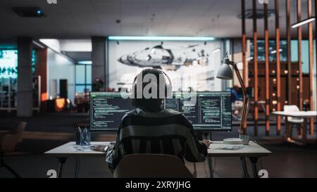 Creative Office: Der professionelle Schwarze Programmierer verwendet Kopfhörer, die auf einem Desktop-Computer arbeiten. Fokussierter Software Engineer, Der Mobile Anwendungen Und Videospiele Entwickelt. Musik hören. Rückansicht Stockfoto