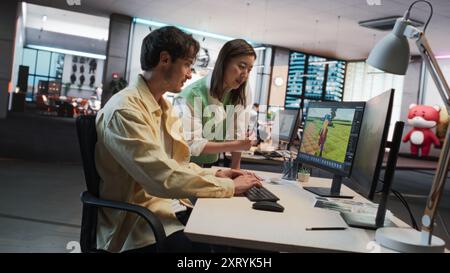 Kaukasischer männlicher Spieleentwickler mit Desktop-Computer mit 3D-Modellierungssoftware und Gespräch mit Asian Female Art Director im Game Development Studio Office. Verschiedene Kollegen diskutieren über das neue Rollenspiel Stockfoto