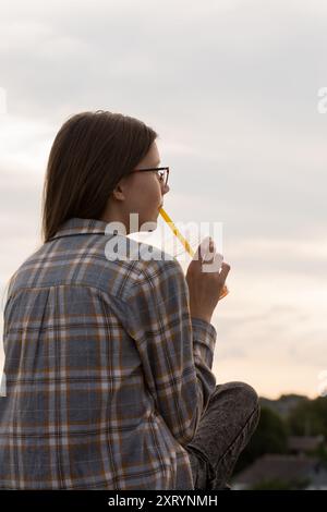 Ein Teenager-Mädchen in Gläsern trinkt Sprudeltee auf einem Spaziergang auf der Stadtstraße Stockfoto