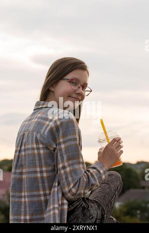 Ein Teenager-Mädchen in Gläsern trinkt Sprudeltee auf einem Spaziergang auf der Stadtstraße Stockfoto