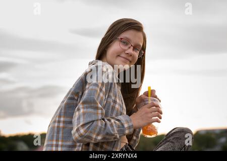 Ein Teenager-Mädchen in Gläsern trinkt Sprudeltee auf einem Spaziergang auf der Stadtstraße Stockfoto