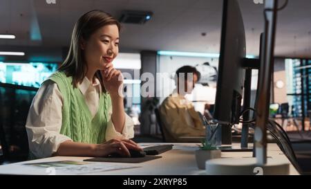 Asiatische Frau, die Desktop-Computer verwendet und in 3D-Modellierungssoftware Unique World und Charaktere für Survival Videospiel in diversen Büros entwirft. Weibliche Spieledesignerin, Die Immersives Gameplay Kreiert Stockfoto