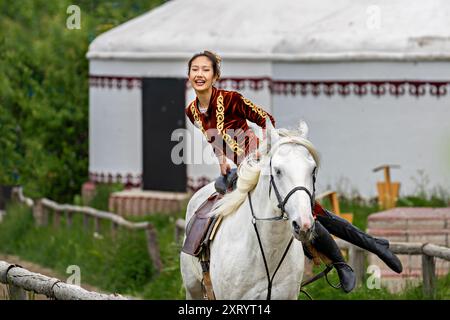 Nomadische Frau, die lokale Kleidung trägt, macht Akrobatik auf Pferden in Almaty, Kasachstan Stockfoto