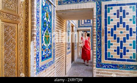 Einheimische Frau in rotem Kleid im historischen Gebäude des Registan-Platzes in Samarkand, Usbekistan. Stockfoto