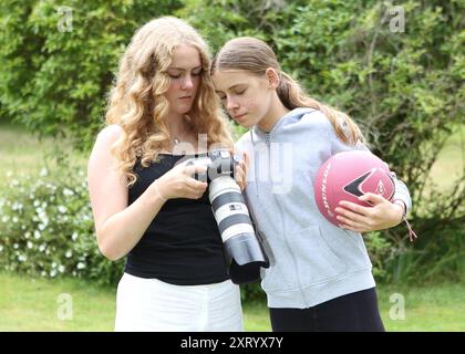 Zwei Mädchen, eines hält einen Netzball, das andere hält eine Kamera mit langem Objektiv und Blick auf die Rückseite des Kamerabildschirms DSLR, um Fotos zu überprüfen Stockfoto