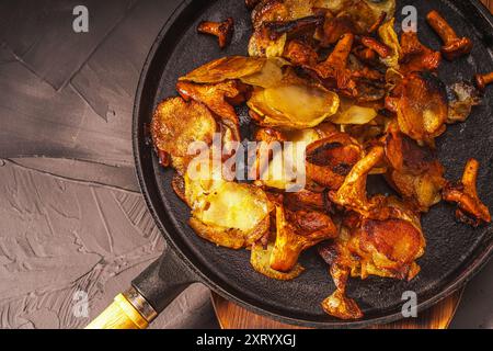 Gebratene Kartoffeln mit Pilzen Chanterellen in einer schwarzen gusseisernen Pfanne mit einer Gabel auf grauem Hintergrund. Hochwertige Fotos Stockfoto