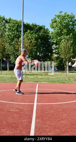 Ein älterer italienischer Mann spielt an einem Sommertag Basketball auf einem Sportplatz. Vertikal Stockfoto