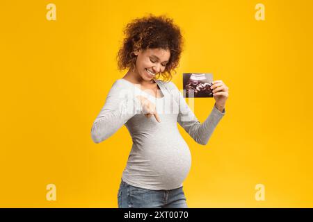 Sehen Sie hier! Angeregte afro-schwangere Frau mit Ultraschalluntersuchung Stockfoto