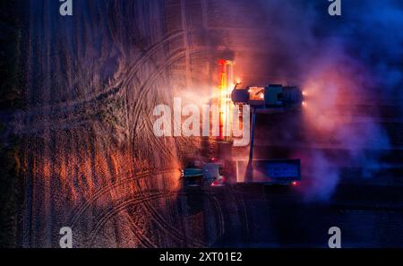 Gadebusch, Deutschland. August 2024. Mähdrescher und Traktorteams fahren nach Sonnenuntergang über ein Feld und droschen Weizen (Foto mit einer Drohne). Nach langen Erntepausen aufgrund von Regen und nassem Boden nutzen die Bauern in Norddeutschland das trockene und warme Wetter, um die letzten Getreidefelder bis spät in den Abend zu ernten. Quelle: Jens Büttner/dpa/Alamy Live News Stockfoto